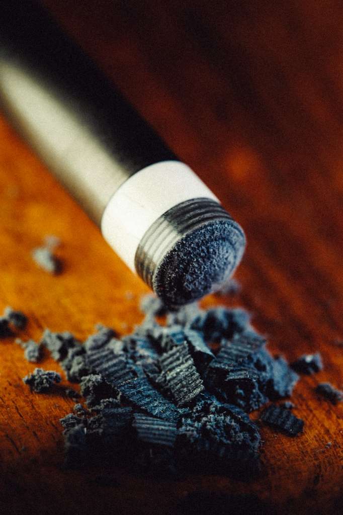 Ghost pool cue tip shaped with debris on a wooden surface